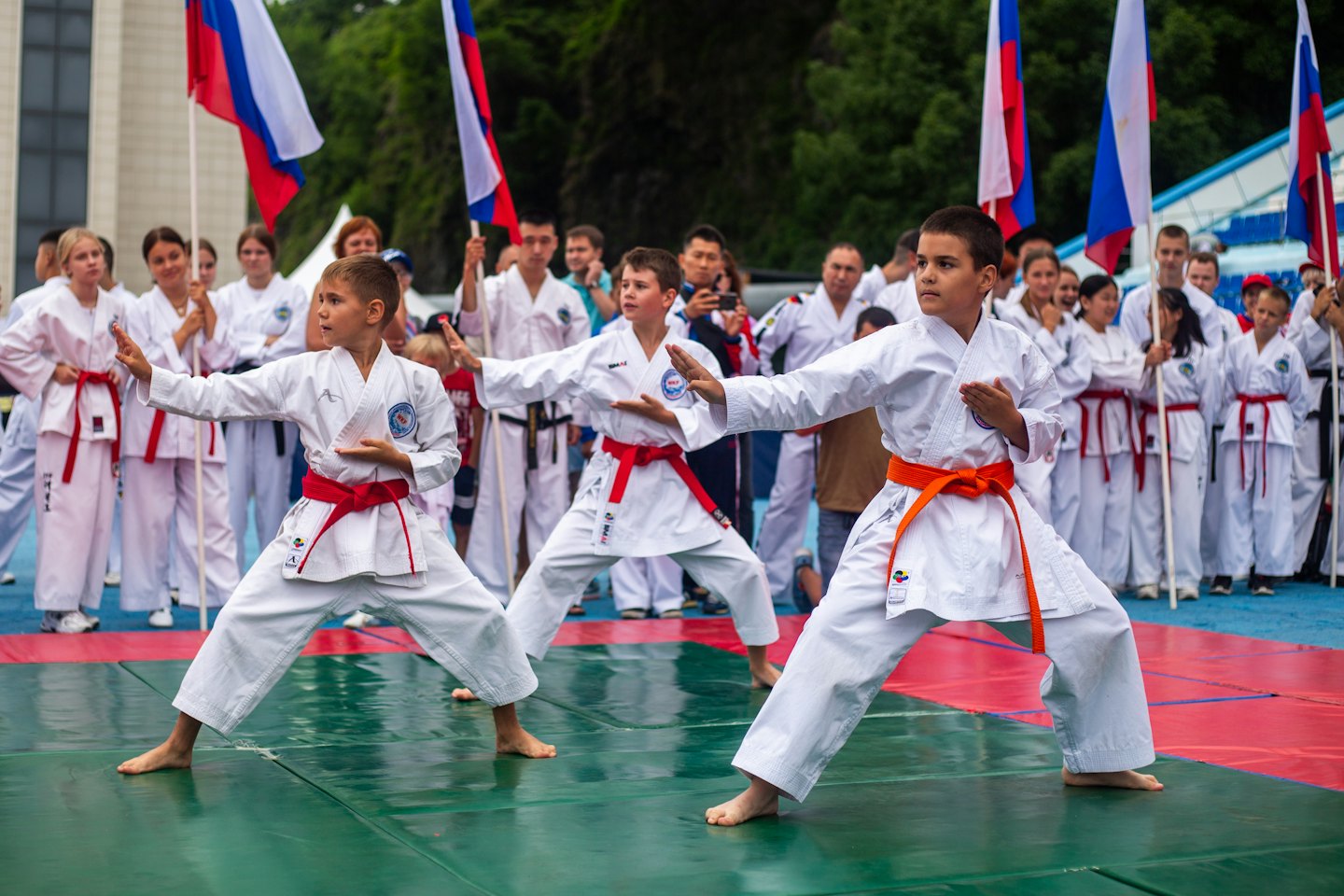 Tre ragazzi in uniforme da karate praticano posizioni sincronizzate su un tappeto.